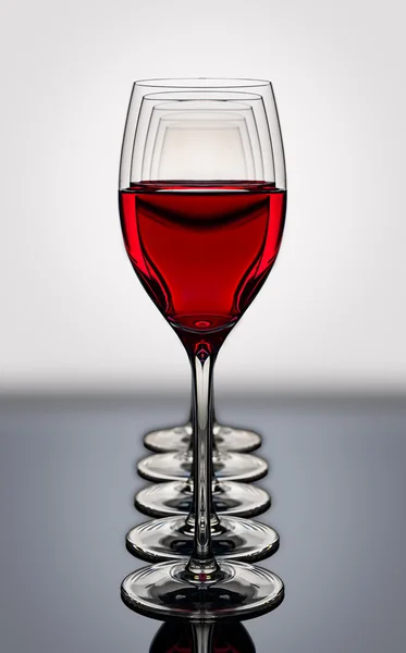 Red wine glasses in a row backlighted on a reflective black boar — Stock Photo, Image