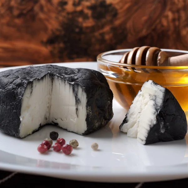 Delicious goat cheese covered with black ash and honey — Stock Photo, Image