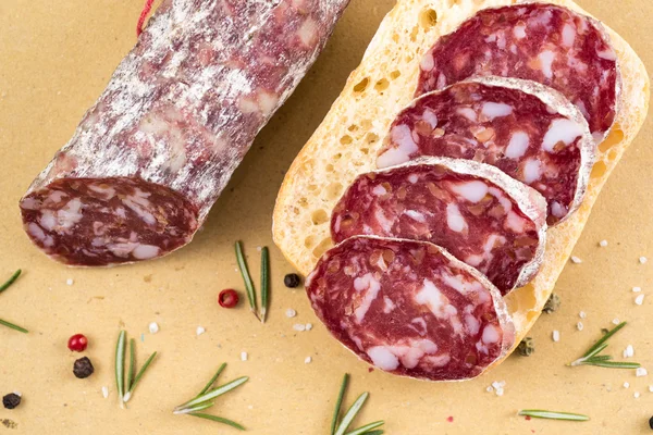 Slices of italian salami on bread and some spices — Stock Photo, Image