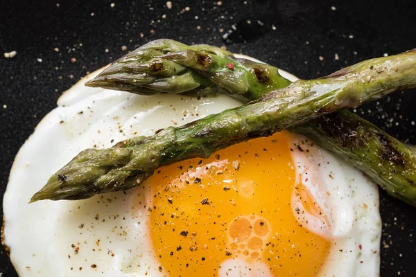 Fried egg and roasted asparagus in black plate — Stock Photo, Image