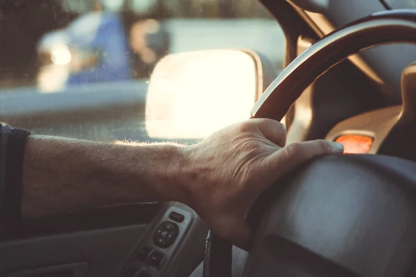 Male hands hold the steering wheel of a car on the road.