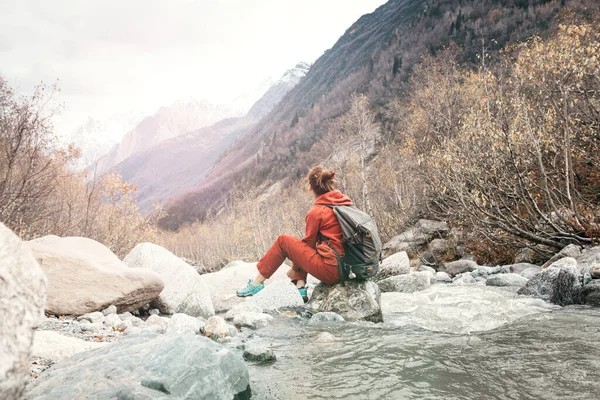 강 옆에 있는 돌 위에 앉아서 산을 구경하는 여자. — 스톡 사진