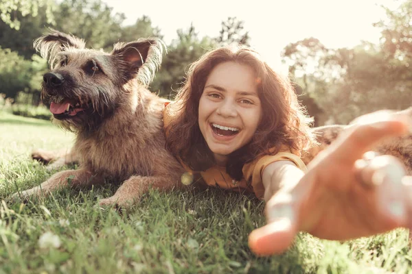 Junge schöne Frau im Gras umarmt den Hund lacht und macht ein Selfie. — Stockfoto