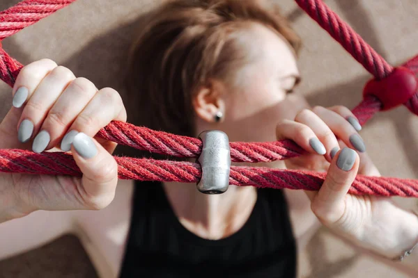 A young woman is lying and her hands are squeezing a red rope. — Stock Photo, Image