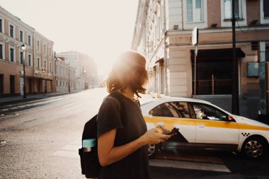 Sırt çantası ve akıllı telefonu olan bir kadın taksi bekliyor..