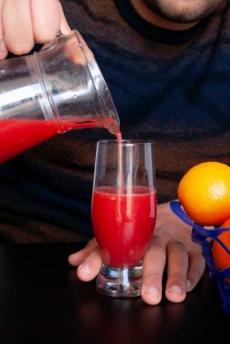 Bir adam portakal suyunu testiden bardağa dolduruyor..