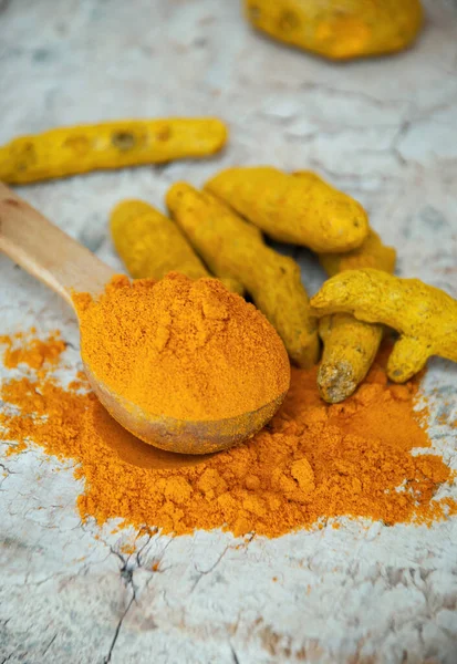Turmeric powder in a wooden spoon next to turmeric roots.