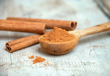 Tarçın tozu, ahşap kaşıkta, tarçın çubuklarının yanında..
