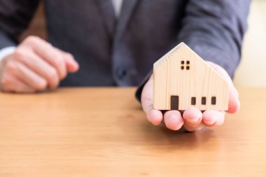 Ahşap evde seçici odaklanma. Emlakçı masada oturuyor ve müşterisine ahşap ev maketi veriyor. Metin için kopya alanı olan ev sahipliği başarı anı kavramı.