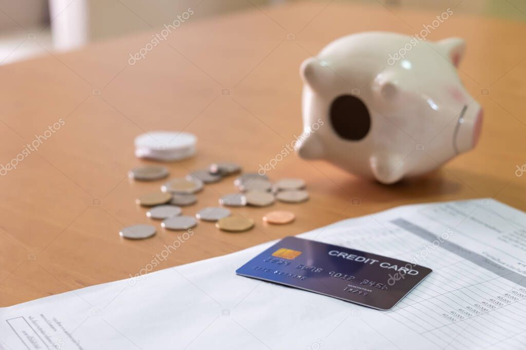 Selective focus at empty piggy bank on the wooden table with blurred coins and Credit card bills payment. Financial problem concept.