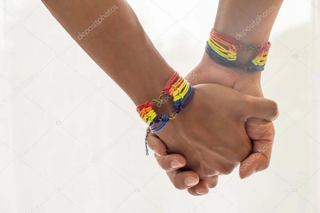 Close up shot of Asian Male couple holding hands with  gay pride rainbow awareness wristbands. LGBT, same-sex love and homosexual relationships with copy space.