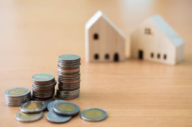 Artan madeni paralar yığınına seçici odaklanma. Bulanık ev, arka plan olarak ahşap masaya oturacak. Ev sahipliği veya emlak satın alma, kredi konsepti için tasarruf planı.