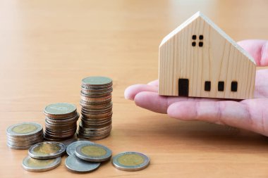 El yapımı ev, artan madeni paraların yanında ahşap masadaki gibi duruyor. Konut veya gayrimenkul mülkiyeti kavramı için başarılı yatırım.