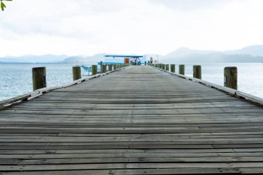 Okyanustaki rıhtıma ya da rıhtıma giden ahşap köprü yolunun açık hava görüntüsü. Arka planda güzel tropikal doğa, gökyüzü, bulut ve deniz dalgalarıyla.