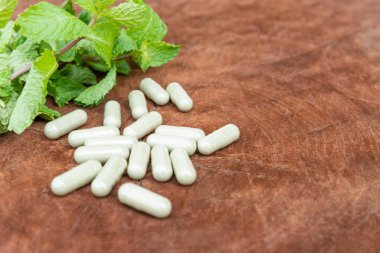 Resmin merkezine seçici odaklanma. Bulanık bitkisel kapsülle doğal ahşap arka planda bitkisel yaprak ve fotokopi alanı. Alternatif tıp hastalıkları tedavi edebilir..