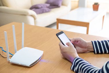 Bilgi ararken akıllı telefon cihazını tutan erkeklere seçici odaklanma, yüksek hızlı internet yönlendiricisinin önünde internette gezinme. Dijital yaşam tarzı için iletişim teknolojisi.