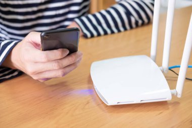 İnternet yönlendiricisinde, evdeki internet veya kablosuz bağlantıya bağlanmak için akıllı telefon aygıtı kullanan bir adamla seçici odak noktası, yüksek hızlı geniş bant ağ kavramı.