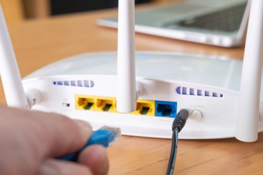 Erkekler arka plandaki bulanık bilgisayar laptopuyla fiber kabloyu sokete bağlarken router antenine seçici odaklanma. Ev kavramında yüksek hızlı geniş bant internet teknolojisi. 