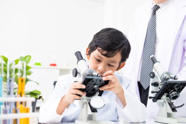 Genç Asyalı öğrenci fen dersinde mikroskop kullanarak konuyu öğretmeniyle birlikte inceledi. Eğitim ve çocukların öğrenmesi veya sınıf konsepti üzerinde deney yapmaları.