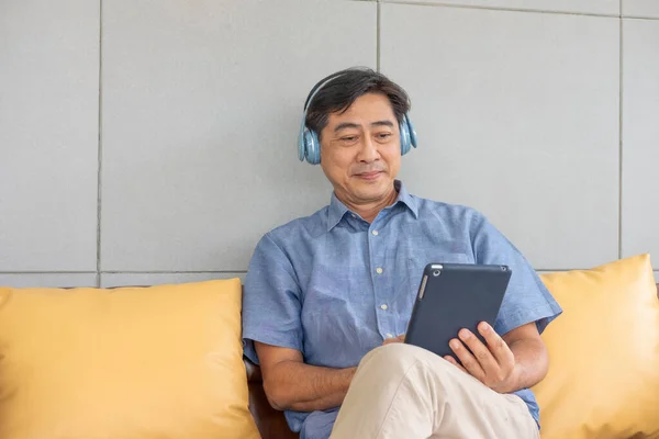 Senior Asian grandfather enjoy and feeling happy while listening music from wireless headphone that streaming music from smartphone or tablet device. Elderly retirement lifestyle with good health.