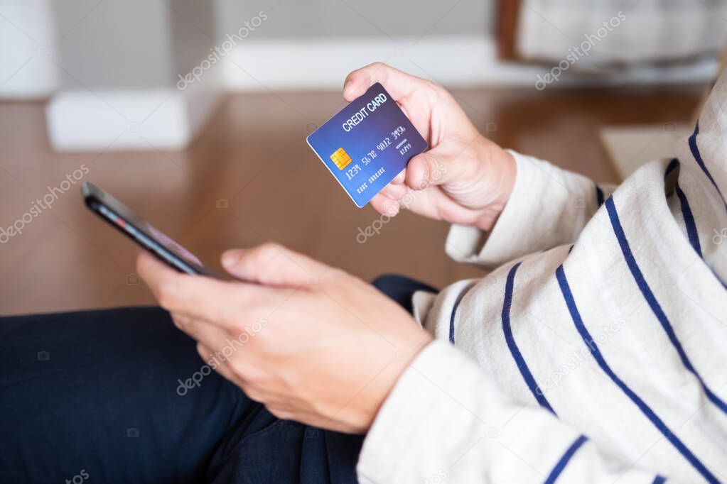Selective focus at men hand holding mobile phone. Close up shot at men while enter security key on credit card for online payment shopping. Wireless banking transaction via internet technology.