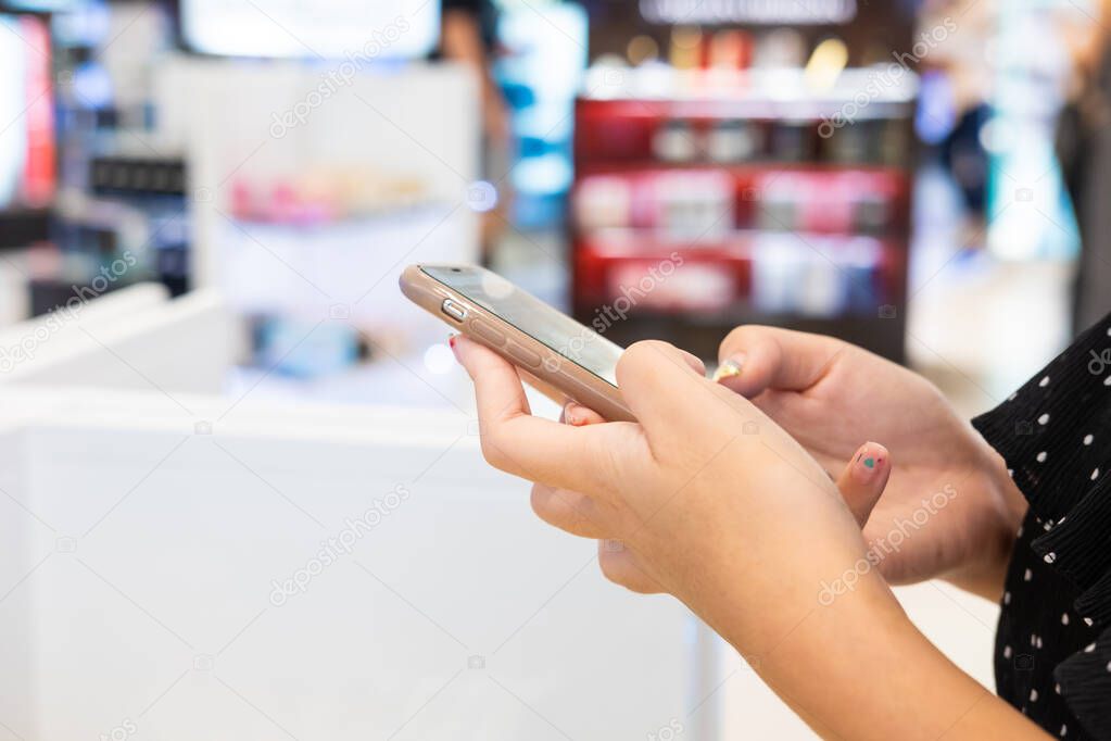 Selective focus at women hand while using smartphone to search for information or get a discount inside department store. Digital coupon that can redeem from mobile device. Technology with business.