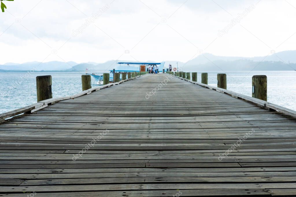 Outdoor perspective shot of wooden bridge walkway down to ship dock or pier in the ocean. With beautiful tropical nature, sky, cloud and sea waves at the background.