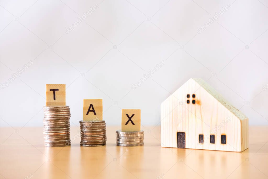 Selective focus at wood tax sign on top of decrease stack of money on the white copy space background. Property or real estate tax payment, expense that need to manage and plan.