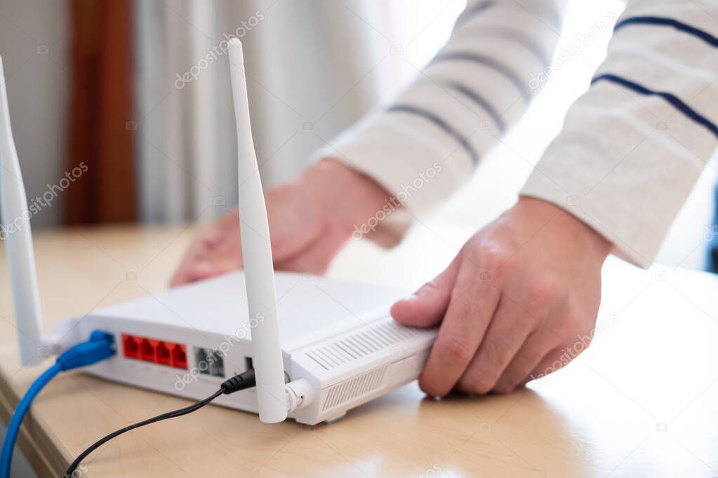 Men hands set up and install broadband high speed internet Wifi router on working table at home. With blue fiber connection line. Telecommunications and digital network technology
