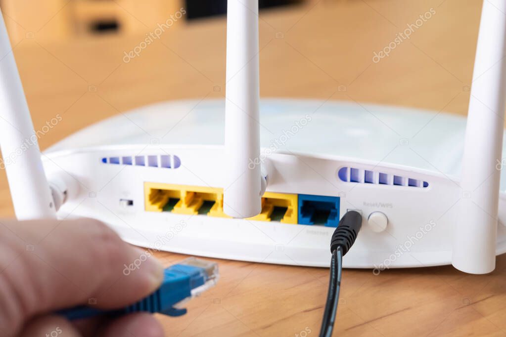 Selective focus at router antenna while men hand connecting fiber cable plug into socket. High speed broadband internet technology at home concept.