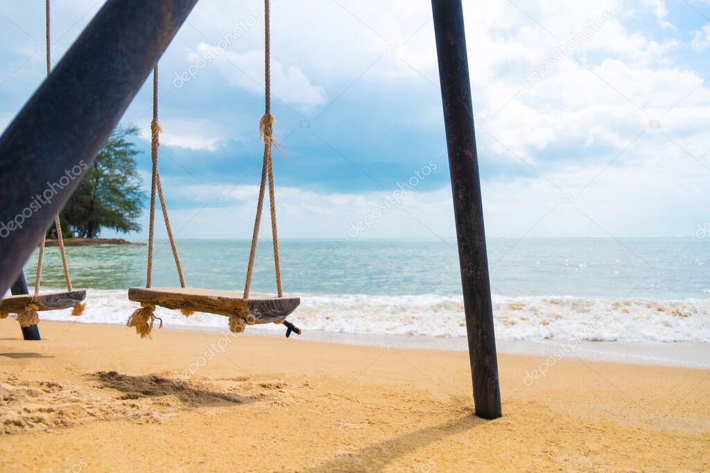 Selective focus at wooden swing on sand at the beach. With wave and sea view with cloud, blue sky. Summer vacation at beautiful tropical island. Travel resort destination.