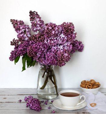 Bir buket leylak ve arka planda bir fincan çay. Bahar çiçekleriyle hayat