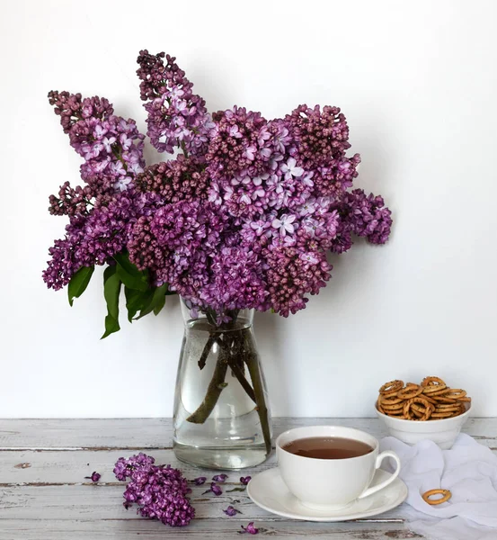 Bir buket leylak ve arka planda bir fincan çay. Bahar çiçekleriyle hayat