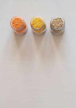 Arka planda kırmızı, sarı ve yeşil mercimek bulunan üç cam kavanoz. Besleyici ve önemli Protein Kaynağı. Düz yatıyordu