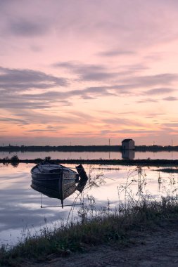 Gün batımında gölde küçük bir tekne, evler, yansımalar, güzel gökyüzü.