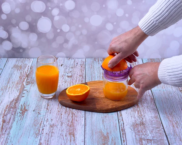 Hand making orange juice, manual juicer, glass on wooden table, glass of juice, wooden floor