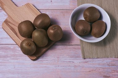 Tahta tahtada ve kasede birkaç kivi var. Tahta tahtalar, zenital manzara, boş alan, beyaz kase, kahverengi masa örtüsü..