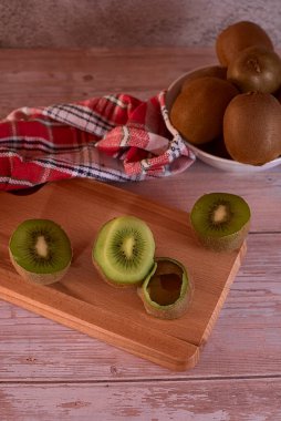 Tahta tahtada derisi olan yarım kiwifruit, bütün kiwifruit ile kase, ahşap döşeme, kırmızı ve beyaz damalı mutfak havlusu