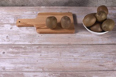 Beyaz kasede ve tahta tahtada çeşitli kiviler. Tahta tahtalar, boş alan, ön manzara, sıcak tonlar.