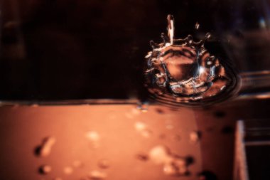 324.su damlacığının yakın plan görüntüsü havada bir taç şekli oluşturuyor. Dalgalar ve kabarcıklar tüm yüzeye yayıldı. Ilık ışıklandırma akışkan hareketi, yansımaları ve dinamik dokuyu vurgular.