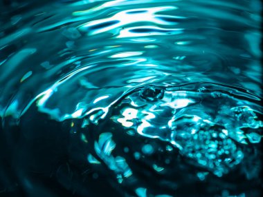 Mavi-yeşil ışıklandırma ve dalgalanma desenleri olan 410.00 'luk yakın çekim su yüzeyi. Yansımalar ve gölgeler akışkan hareketi vurgular. Görüntü dokuyu, dalga davranışını ve ışık bozulmasını yakalar.