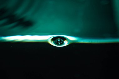 392.Sıvı yüzeye yakın çekim, mavi-yeşil ışıklı tek bir kabarcık gösteriyor. Baloncuk kısmen su altında. Işık yansımaları ve kırılma, yüzey gerilimini ve sıvı dokusunu vurguluyor.