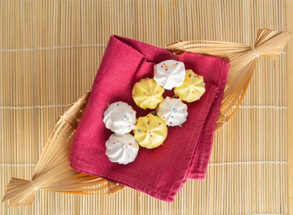White and yellow Meringue cakes on a red napkin in a wicker vase — Stock Photo, Image