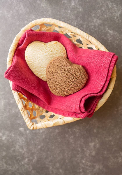 Light and dark cookies in the shape of hearts on a red linen napkin in a wicker vase in the shape of a heart, copy space on a dark background — Stock Photo, Image