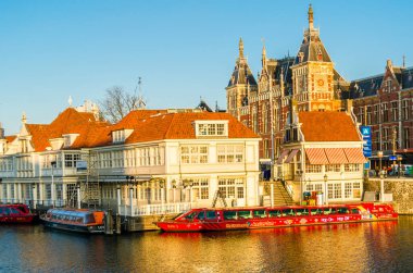 AMSTERDAM, NETHERLANDS - 17 Kasım 2018: Amsterdam 'daki merkezi tren istasyonu görüntüsü ve turist botları için bir rıhtım