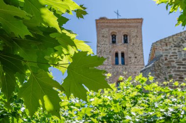 İspanya, Madrid 'de Buitrago del Lozoya' daki Santa Maria del Castillo Kilisesi 'nin Mudejar kulesinin uçak ağaçlarının olduğu parkın manzarası.