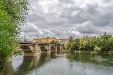 İspanya, La Rioja, Logrono 'daki Ebro Nehri' nin gündüz manzarası, nehir kenarındaki binalar ve gri bulutlu gökyüzü sakin bir şehir manzarası yaratıyor.