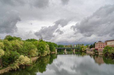İspanya, La Rioja, Logrono 'daki Ebro Nehri' nin gündüz manzarası, nehir kenarındaki binalar ve gri bulutlu gökyüzü sakin bir şehir manzarası yaratıyor.