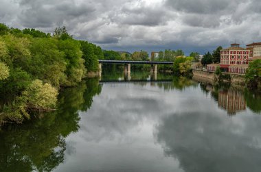 İspanya, La Rioja, Logrono 'daki Ebro Nehri' nin gündüz manzarası, nehir kenarındaki binalar ve gri bulutlu gökyüzü sakin bir şehir manzarası yaratıyor.