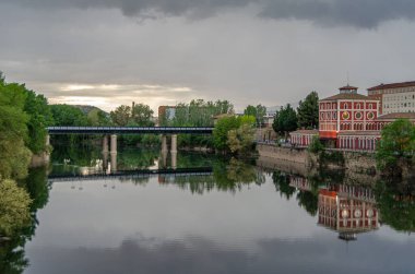 İspanya, La Rioja, Logrono 'daki Ebro Nehri' nin alacakaranlık manzarası nehir kenarındaki binalar ve sıcak akşam ışığı suyu yansıtıyor.